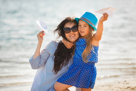 年轻母亲和女儿在海滩上玩纸飞图片
