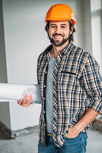 身着格子衬衫和安全帽的成功微笑建筑师站在有蓝图的建筑屋图片