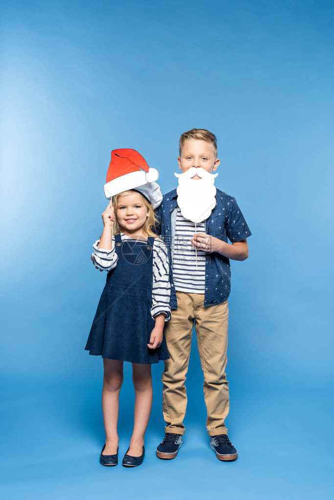可爱的小男孩女带着圣塔帽和假胡子在摄图片
