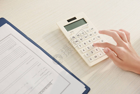 妇女在带有保险索赔表的桌子上用计算器计算财图片