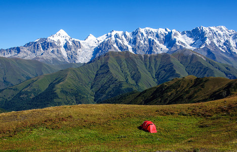 在高加索山雪峰背景的红色旅游帐篷上搭图片