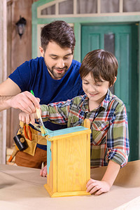 快乐的父亲和儿子在车间中画木制图片