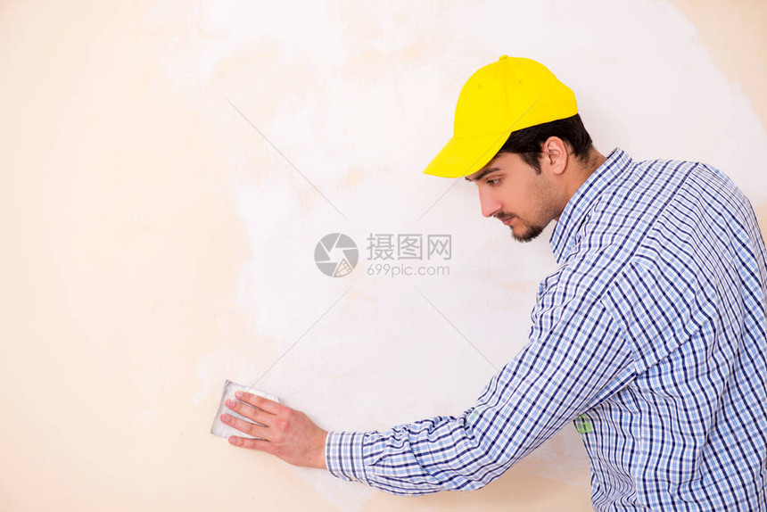 年轻承包商用砂纸打磨墙壁图片