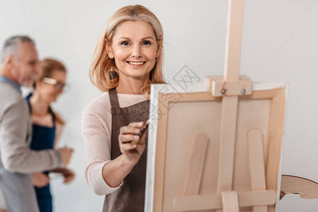 美貌丽的成熟女子在艺术课的壁架上绘画时图片