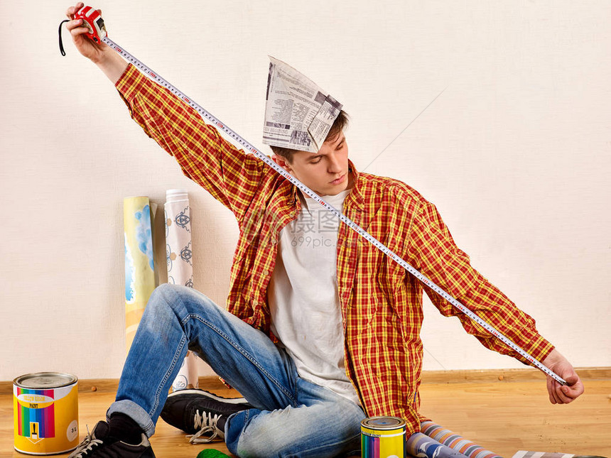 修理家的人做测量男拿着卷尺的墙纸他在报章装修的公寓里油漆库和油漆刷靠近墙壁工图片
