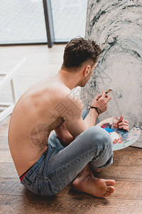 半裸艺术家盘腿而坐在画廊绘画图片