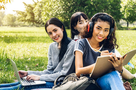 一群微笑着的国际学生或青少年在大学公园里一起用笔记本电脑做功课图片