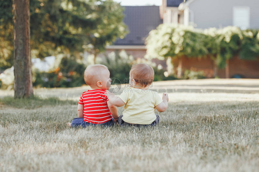两个可爱的白种人小婴儿一起坐在外面的田野草地上从后面看夏日公园里快乐的小孩子们在日落时分与朋友图片