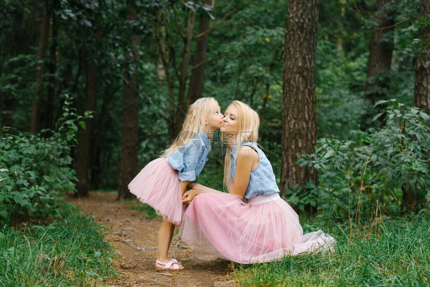 一位母亲和一个五岁的女儿穿着同样浪漫的衣服在公园或树林里散步我的女儿亲吻图片