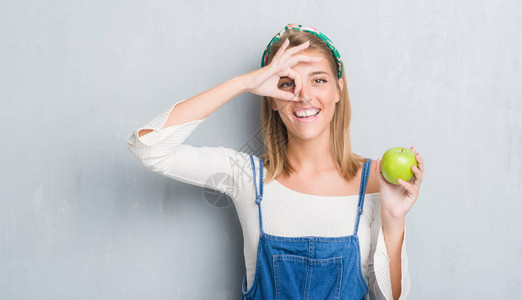 美丽的年轻女子在垃圾灰色的墙上吃着绿色的苹果图片