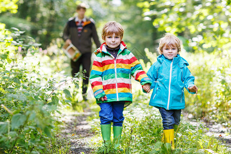 两个小兄弟穿着多彩防水雨衣和橡皮靴在秋天的森林图片