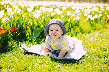 施莱尔沃肯快乐微笑的女婴躺在郁金香田野绿草的毯子上孩子在春天公园户外玩耍母亲节背景