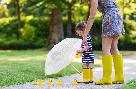 可爱的两年女孩穿着黄雨靴在夏令背景图片