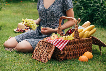 妇女吃葡萄和野餐时坐在绿草地图片