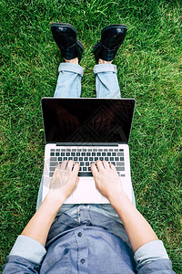 坐在绿草地上用空白屏幕的笔记本电脑背景图片