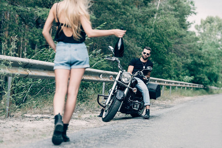 年轻女子在路上骑着黑色摩托车在男友身边带着一瓶酒走图片
