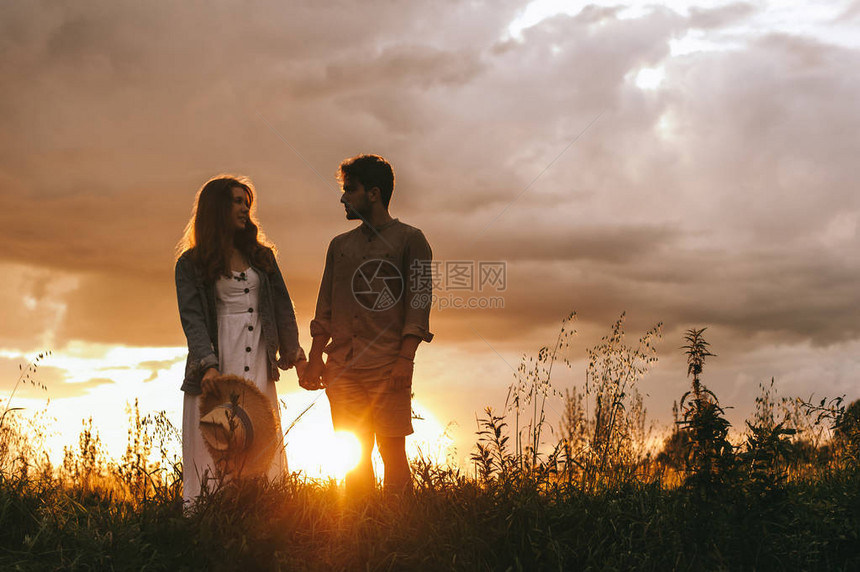日落时在草地上牵手的情侣剪影图片