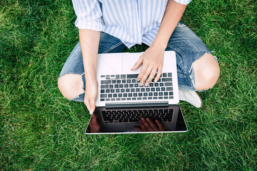 坐在草地上时用空白屏幕的笔记本电脑对年轻图片