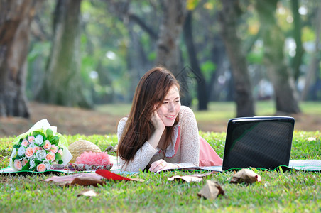 妇女坐在木垫上在公园里看笔记本电脑图片