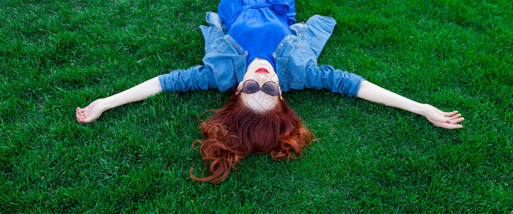 美丽的红发女人在夏天躺在绿草地上图片