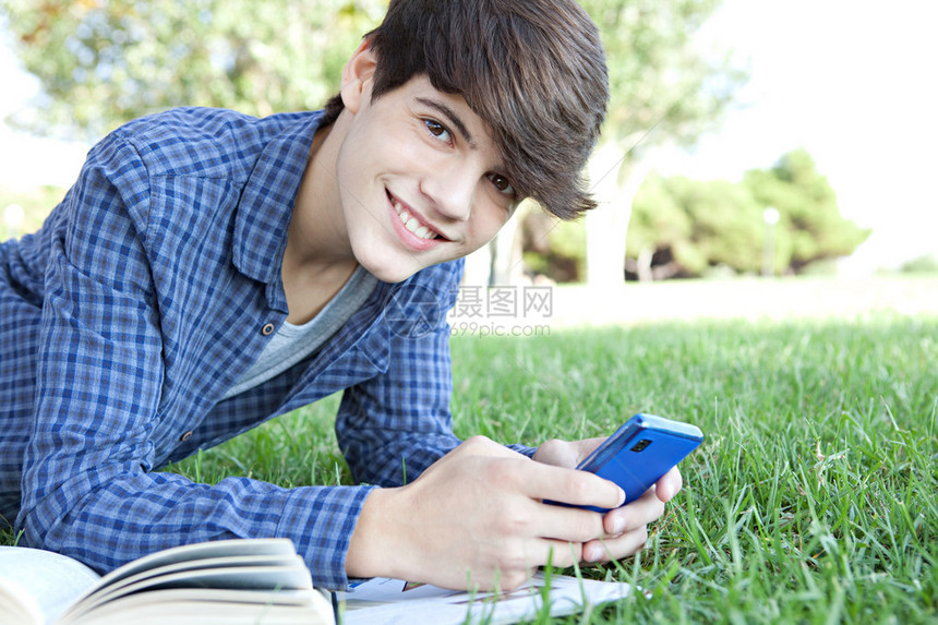 侧面肖像特写视图一个年轻的少年学生男孩躺在公园里他的大学书籍并使用智能手机浏览互联网图片