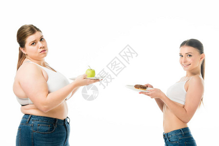 快乐的苗条女人和超重的女人在与白色隔离的盘子上摆着甜图片