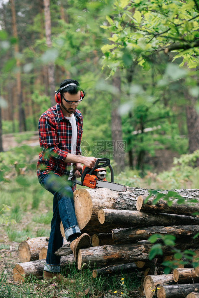 戴耳膜和防护眼镜的伐木工人用连链锯在森图片