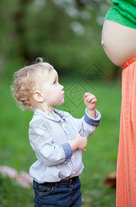 可爱的小男孩在户外看着怀孕的母亲的肚子他期待图片