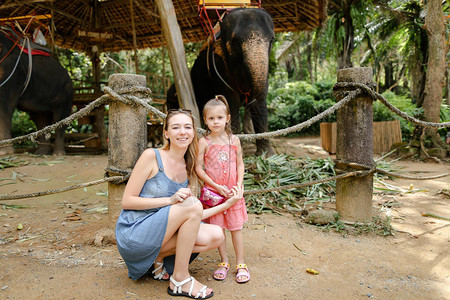 年轻女子带着小女儿站在驯服和绑大象附近带着孩子去异国他乡和野生驯养动图片