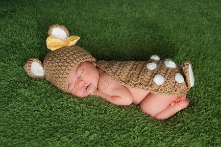 一名新生的女婴穿着白尾鹿牛装睡在青绿背景