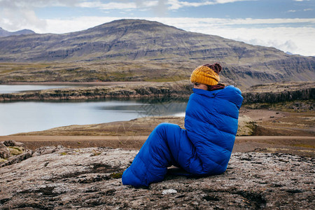 身着温暖蓝睡袋的年轻女子在冰岛北背景图片