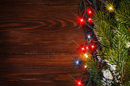 圣诞树枝和木背景上的彩色灯光用图片
