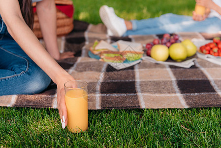 野餐时坐在格子上用新鲜果汁装着玻璃杯的人图片