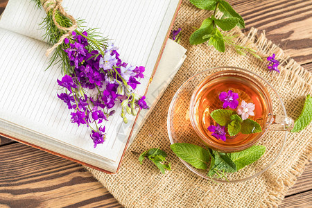 玻璃杯夏季凉茶与新鲜薄荷和田野飞燕草笔记本上的野花束木图片
