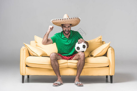穿着墨西哥草帽的快乐男人坐在黄色沙发上看足球比图片