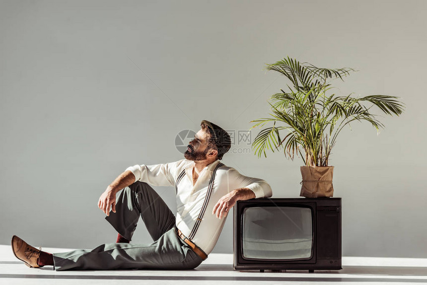 长着英俊胡子的男子坐在老旧电视旁边的地板上图片
