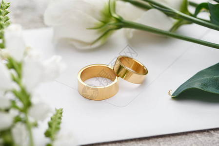 白枯叶花旁白色信封上的结婚戒指有图片