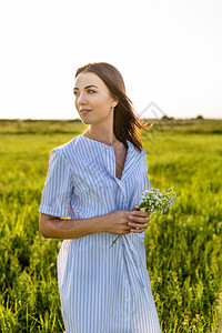身着白衣服的年轻美女与田野鲜花束在背景图片