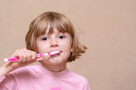 在浅色背景上刷牙粉红色牙刷的女孩图片