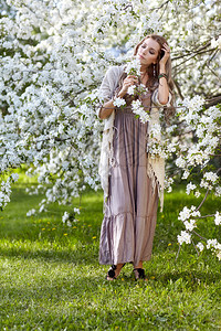 穿着长裙子的漂亮年轻女子在春花园鲜花中的苹果树下图片