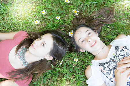 有趣的女孩双胞胎姐妹少年躺在草花上图片