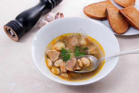 白碗中的豆汤和轻石背景的金属勺子图片