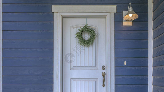 挂在蓝色家的白色门上的花圈挂在家里的白色木制前门上的花圈房子有一个蓝色的外墙背景图片