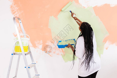 快乐微笑的非洲裔美国女人画新房子的内墙重新装修整修公寓修背景图片