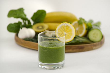 绿色冰沙碱饮食料与新鲜柠檬旁边的木制托盘与碱饮食蔬菜和水果背景图片