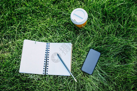 用铅笔带空白屏幕的智能手机和绿草坪上的一次咖啡杯对图片