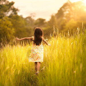 小女孩在日落的草地上奔跑图片