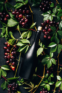 绿色树叶和黑木面上酒瓶子的亮新熟葡萄图片