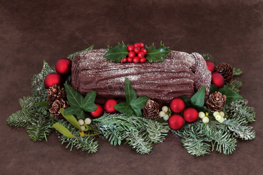巧克力圣诞原木与红色摆设装饰冬青常春藤槲寄生积雪的冷杉和松果在棕色手工制作的lok图片