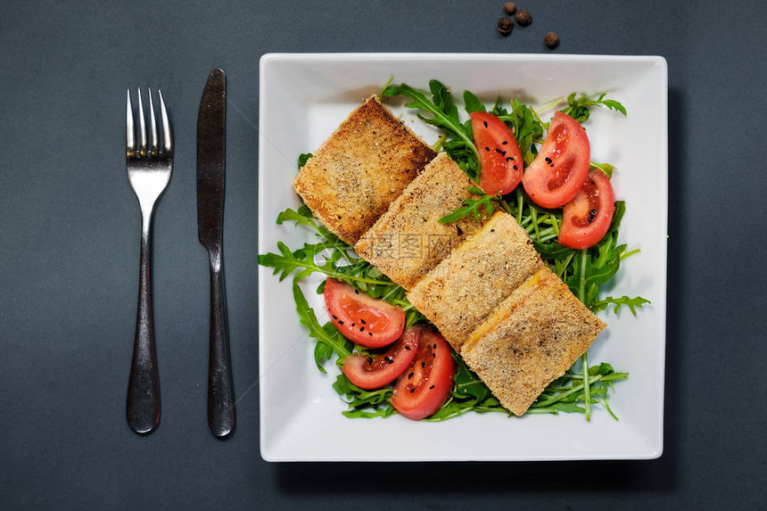 炸豆腐沙拉配西红柿和罗库拉黑色背景上的白盘子里的自制素食沙拉一种健康的亚洲饮食图片